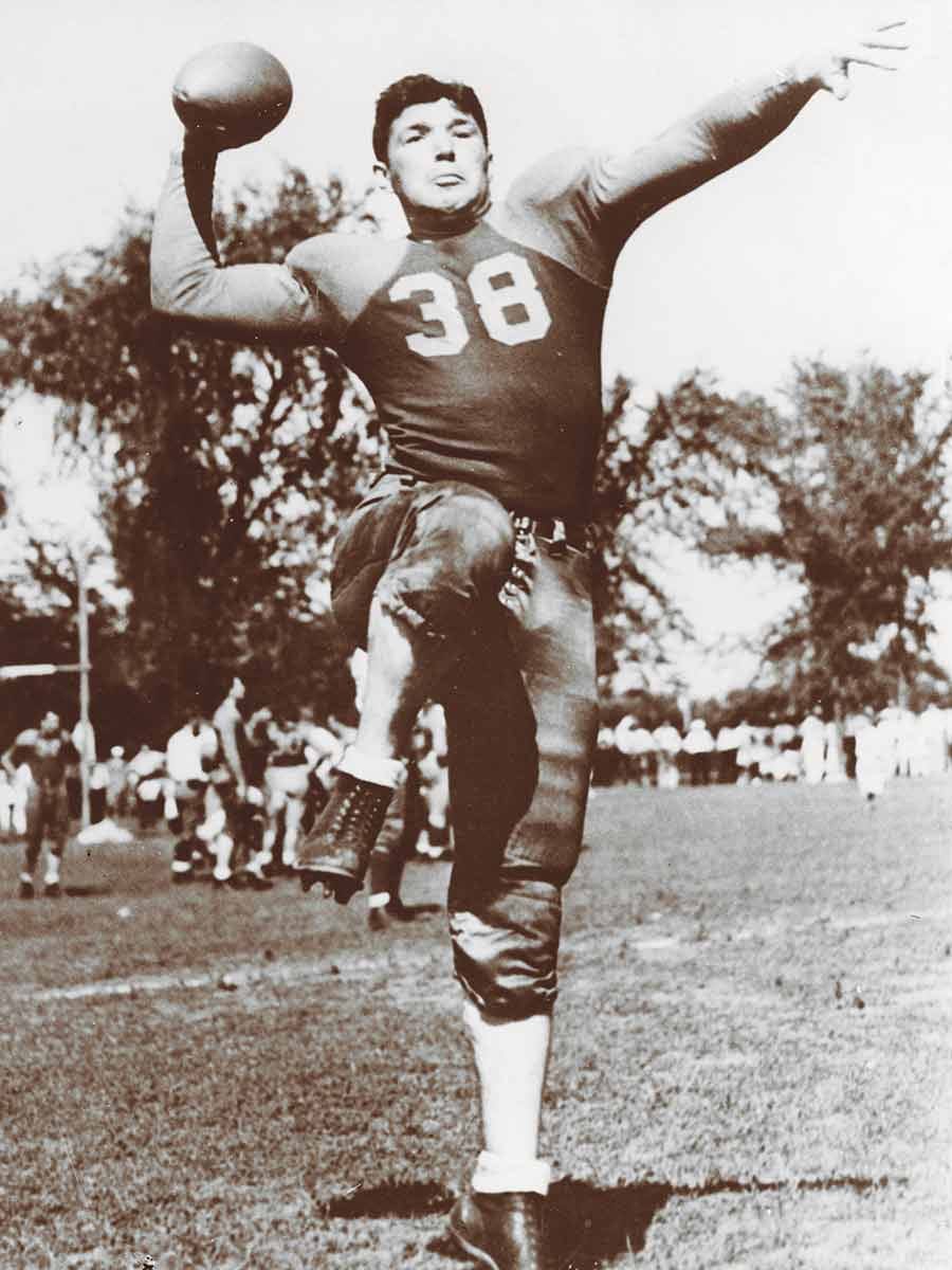 Arnie Herber in a full football uniform, putting his right leg up and aiming to throw the football.