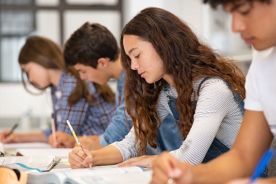 Four teenagers sit at a classroom table and write.