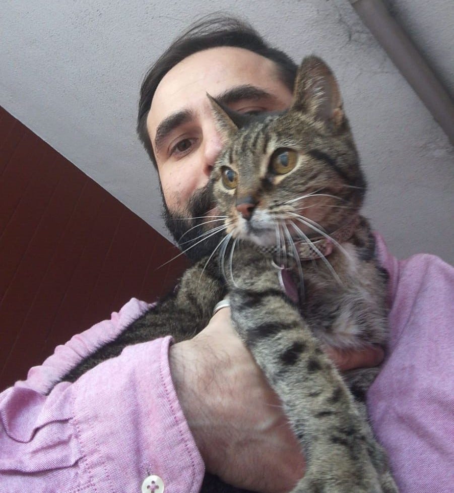A man in a soft pink shirt holding a tabby cat to his chest
