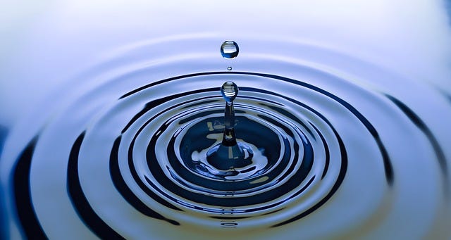 A drop of water splashing into a water pool creating a ripple effect