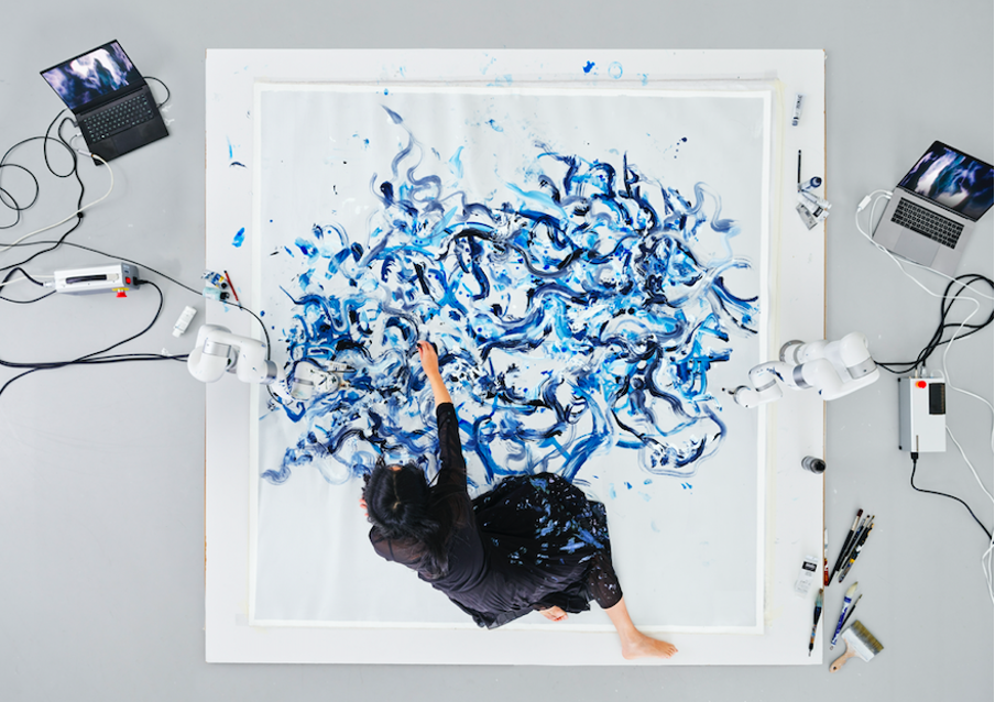 top view of Sougwen Chung using hybrid intelligence to create a two dimensional painting