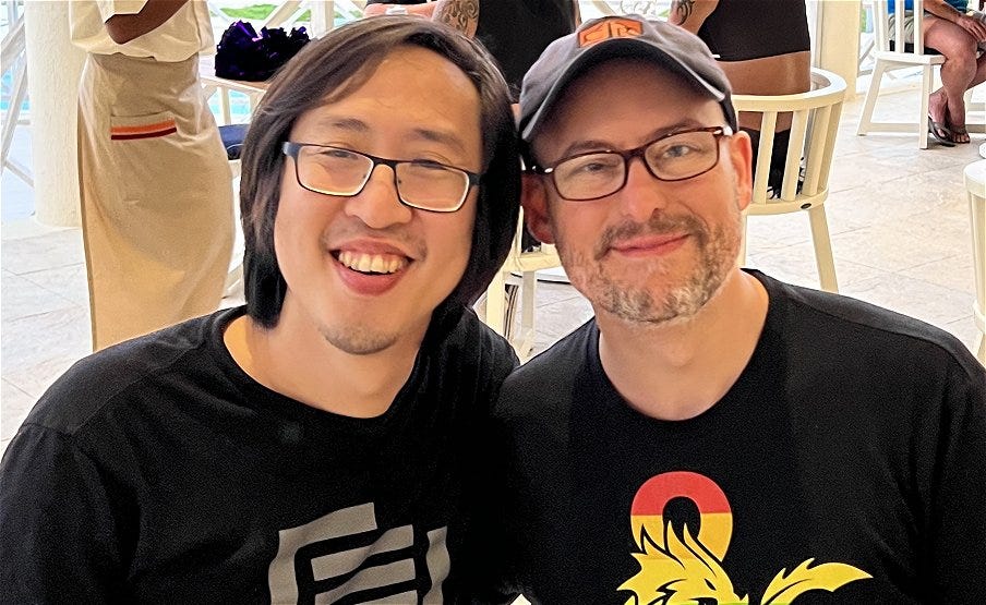 Two smiling men, one with a rainbow ampersand dnd shirt