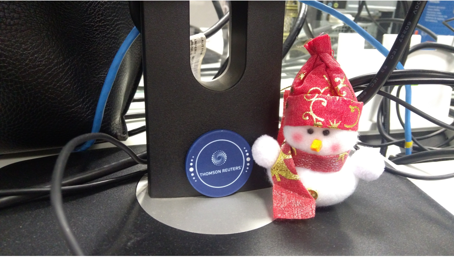 Base de um monitor preto, um boneco de neve branco com gorro e cachecol vermelhos e um circulo azul escrito Thomson Reuters em branco.