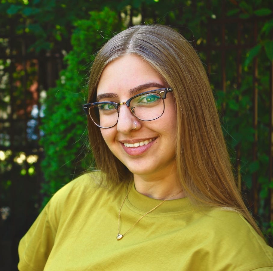 Rojhan Paydar smiling into the camera. She is wearing a lime green t-shirt dress, has glasses, a nose ring, and great brows