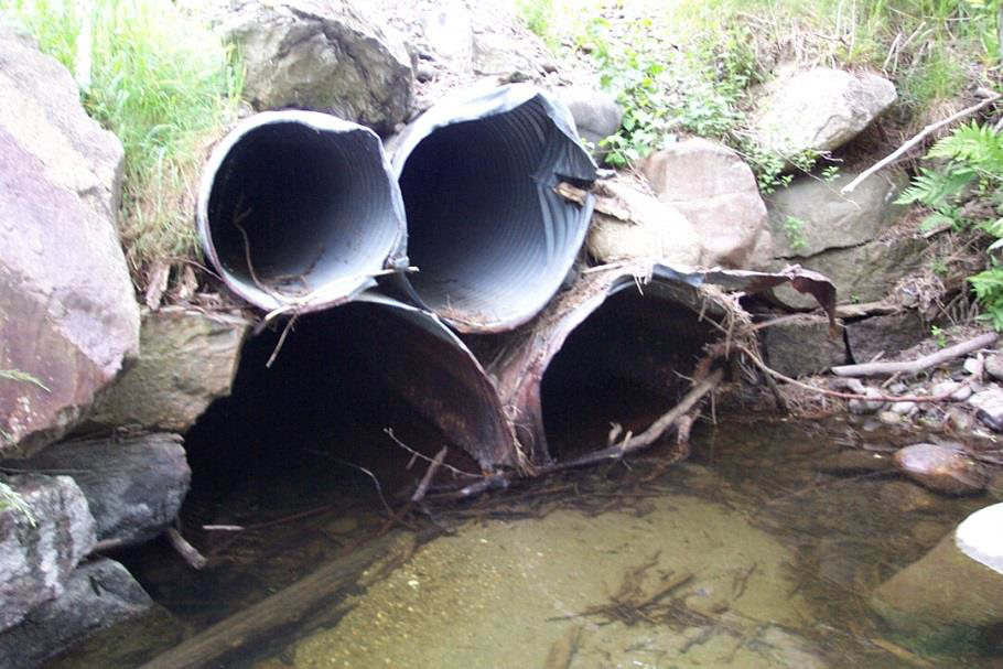 Four bent pipes under a road, partially in a stream