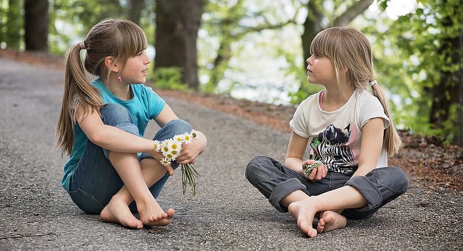 Two young girls talking while sitting on pavement.