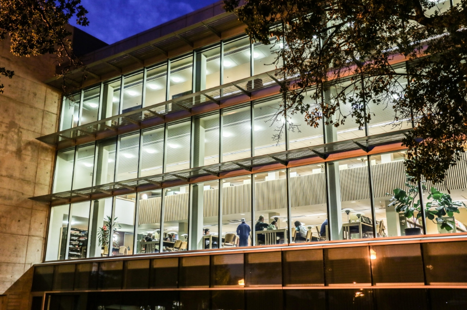 A photo of busy students inside Wardman Library during the evening. This picture is taken from the outside emphasizing the lights from within the library.