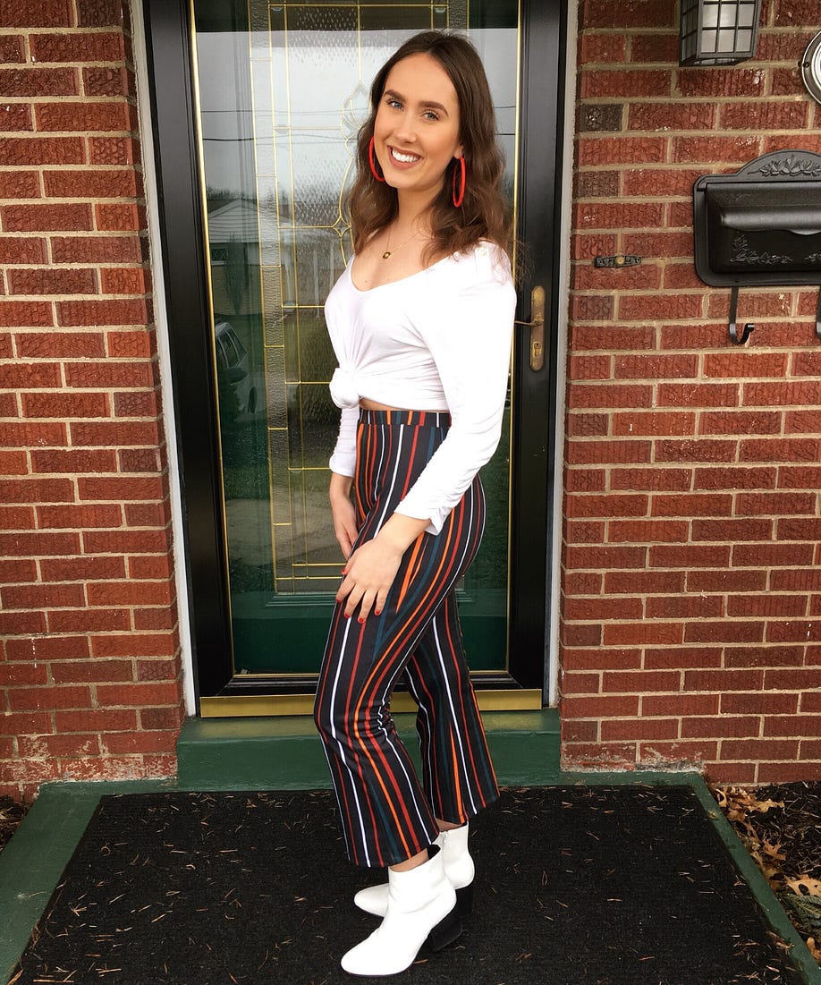 Me wearing a white top with black flarred pants with colored stripes and white ankle boots.