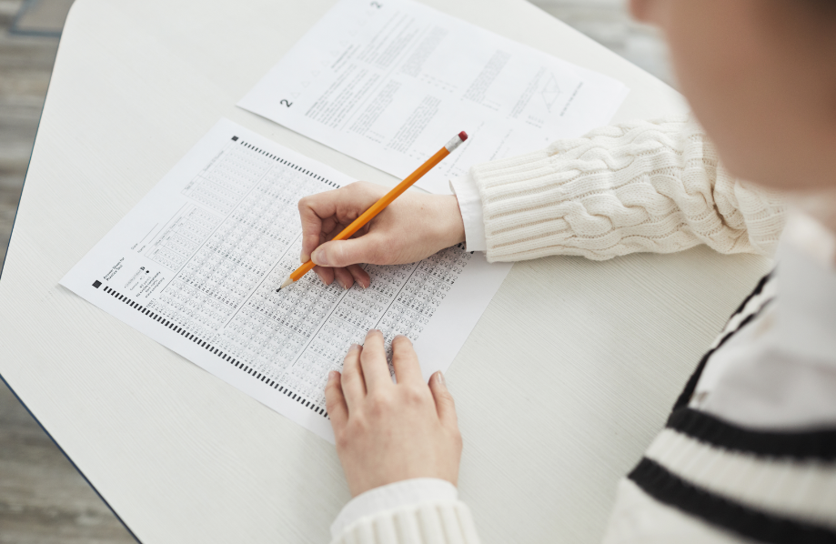 A student fills in answers on a paper test with a pencil.