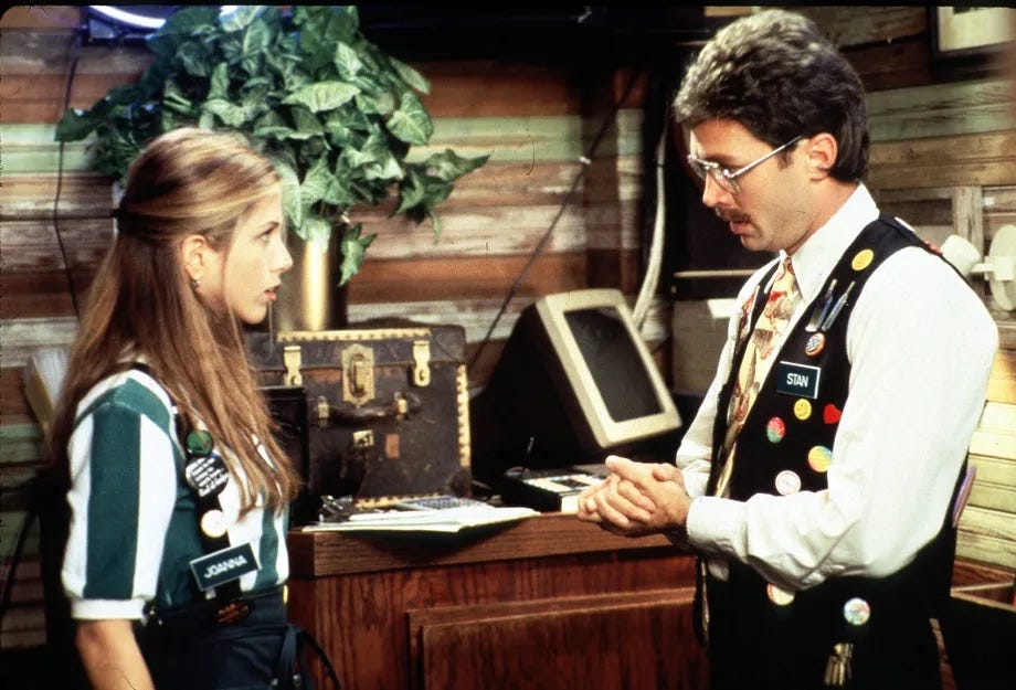 A scene from the movie Office Space, showing Jennifer Aniston getting reprimanded about her pieces of flair.