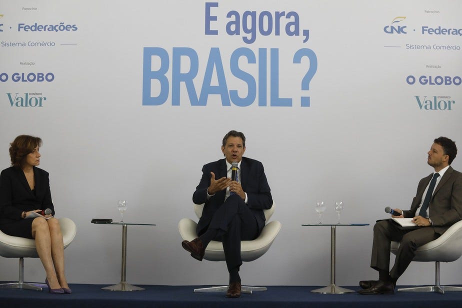 Descrição: na imagem temos a Jornalista Míriam Leitão, à esquerda, o ministro da Fazenda, Fernando Haddad, no meio e à esquerda o jornalista Fernando Exman. Todos estão sentados e o evento ocorreu no último programa ‘E agora, Brasil?’ do Jornal Globo/Valor Econômico.