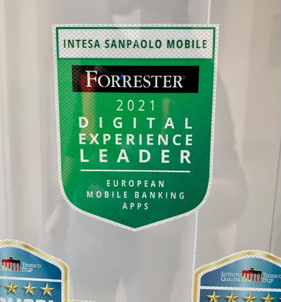 Il badge che Forrester ha assegnato a Banca Intesa Sanpaolo, incollato al vetro della porta d’ingresso. Riporta il logo di Forrester posto sopra la scritta “2021 Digital Experience Leader — European Mobile Banking Apps”.