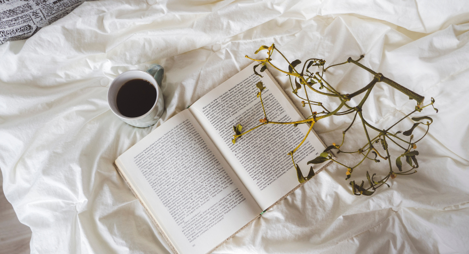 A cozy reading setup featuring an open book lying next to a dried plant and a cup of coffee, all arranged on a clean, white surface, inviting a moment of relaxation and intellectual engagement.