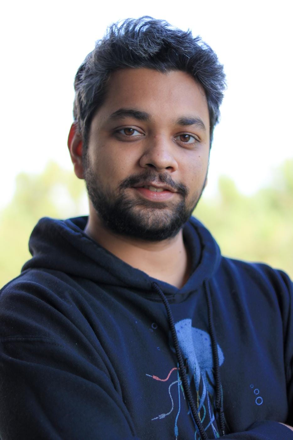 Headshot of Manaswi Mishra. He is looking directly into the camera, and wearing a blue hoodie with a colorful logo that looks like an octopus made of electronic components.