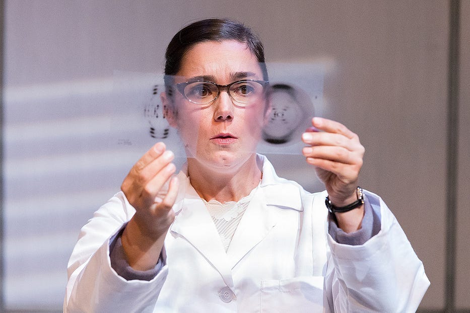 A woman with brown hair in a lab coat holds up two transparent slides with images of DNA