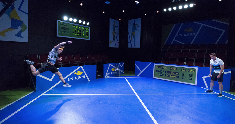 Two actors “play” tennis on a stage set up to look like a tennis court