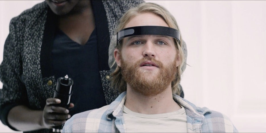 Imagem mostrando a cena de um dos episódios da série Black Mirror, onde há uma mulher com um dispositivo na mão atrás de um homem, que tem um um outro dispositivo circulando sua cabeça.
