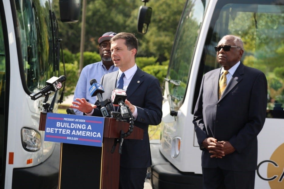 Secretary Buttigieg delivers remarks with Majority Whip Clyburn with two electric buses in the background.