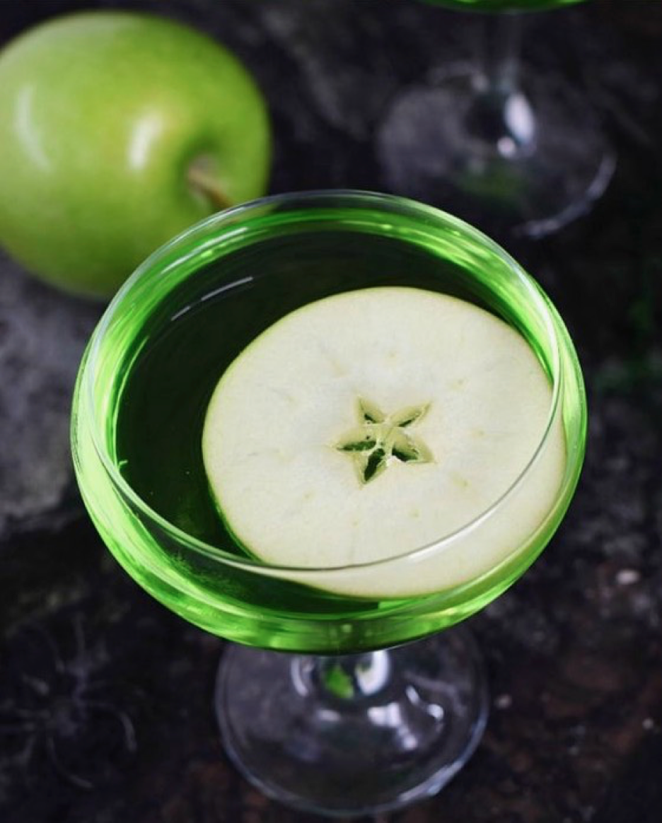 Image of bright green cocktail with a floating apple slice.