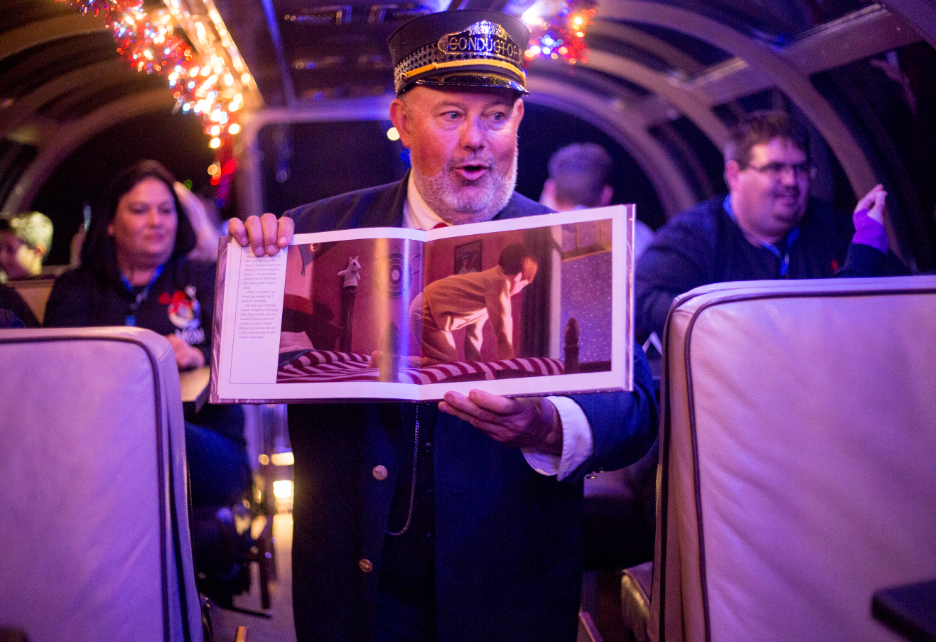 The train conductor holds up a copy of The Polar Express as he walks through the car.