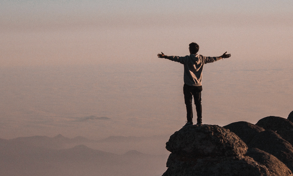 Man standing with arms spread out wide at edge of mountain