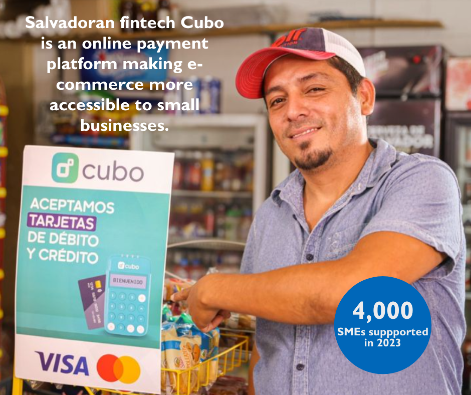 Man with baseball hat with small smile pointing towards a Cubo sign in a convenience store.