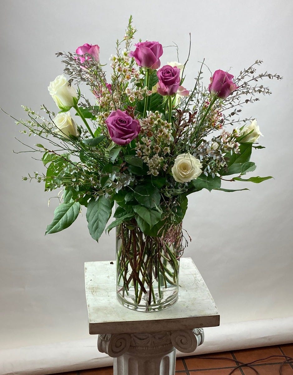 A dozen roses in a vase. Six hot pink roses and six white roses. It has accents of wax flower and greenery.