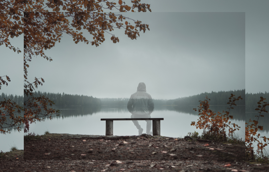 A a transparent person in a hoodie with his back to us, sitting on a bench overlooking a lake.