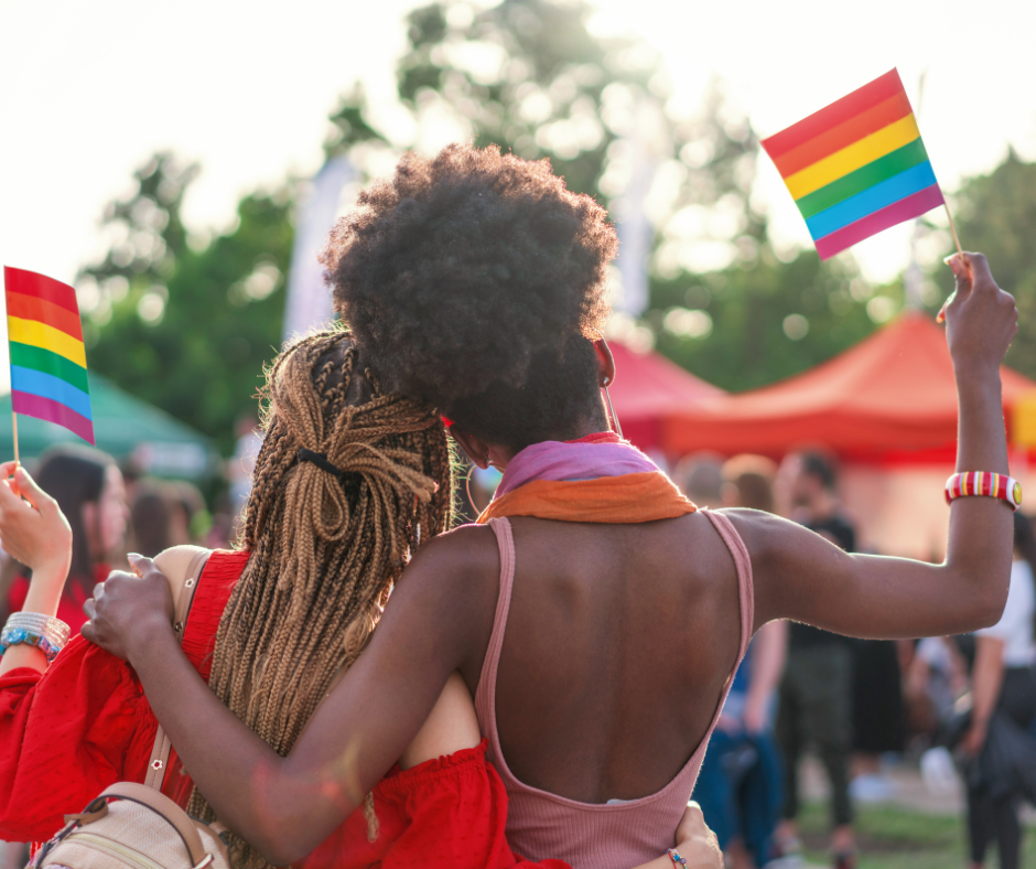 Two BIPOC individuals waving pride flags.