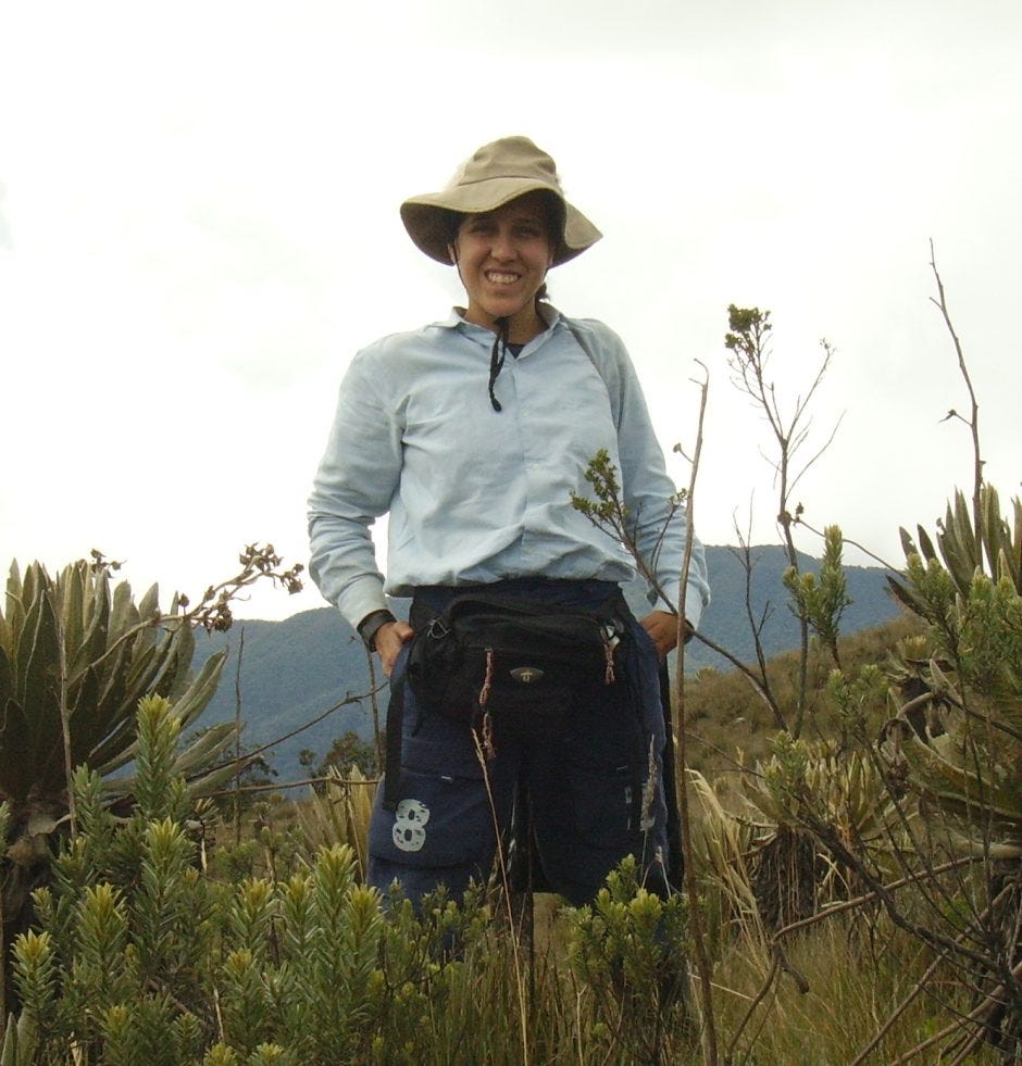 A woman stands smiling in a shrubby landscape