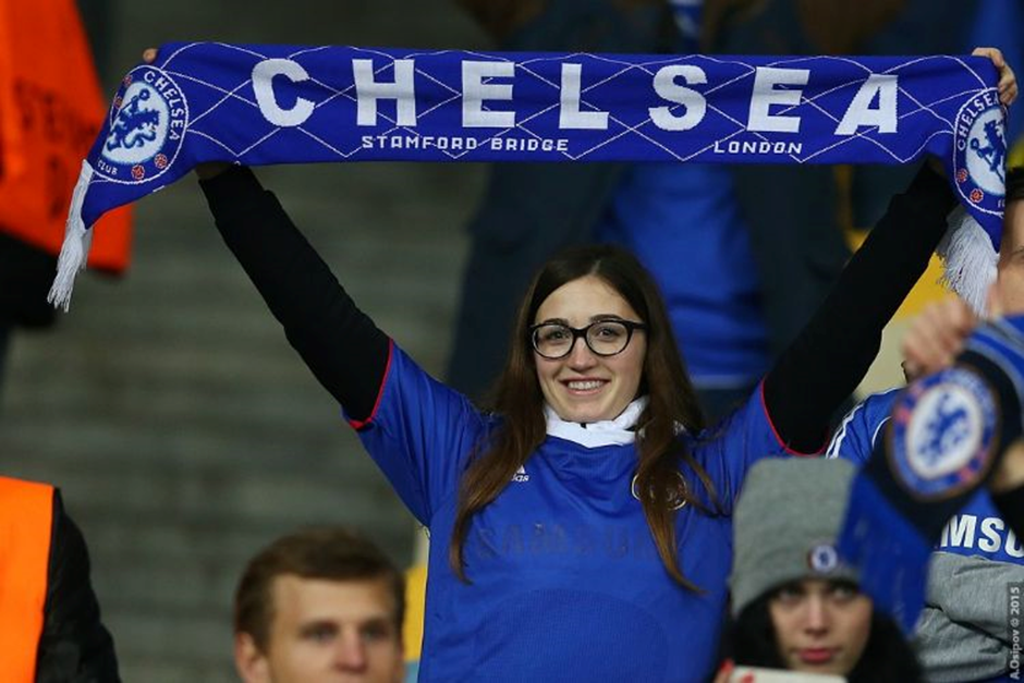 A female Chelsea fan holding a blue scarf of the club high above her head