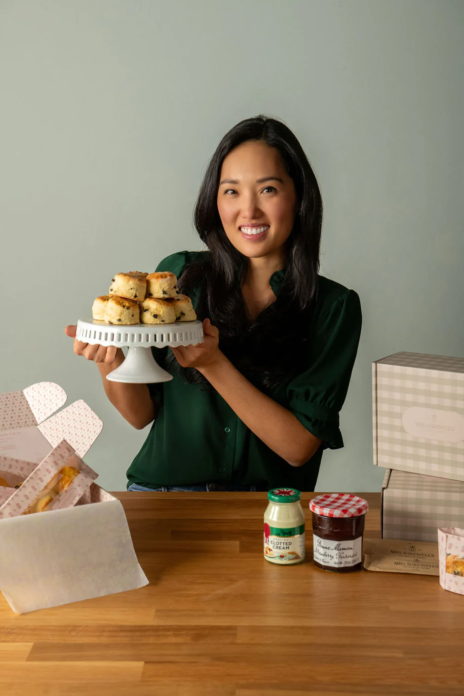 smiling woman holding a cake plate piled with scones