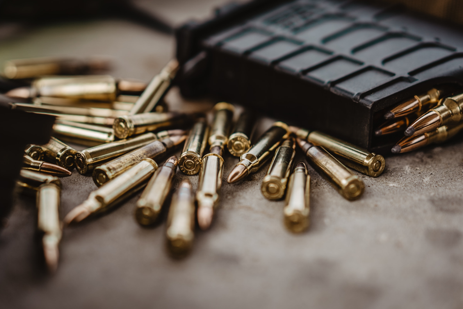 Shiny brass-colored bullets strewn haphazardly on a table next to a grey cartridge loaded with the same ammunition.