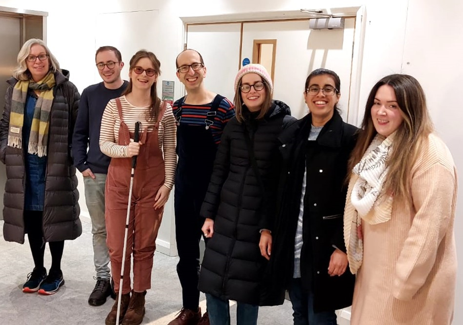 7 people standing in height order. They look joyful, with expressions ranging from bemused to happy. The 2 content designers, Jack and Chloe are both wearing dungarees and striped tops as an act of solidarity.