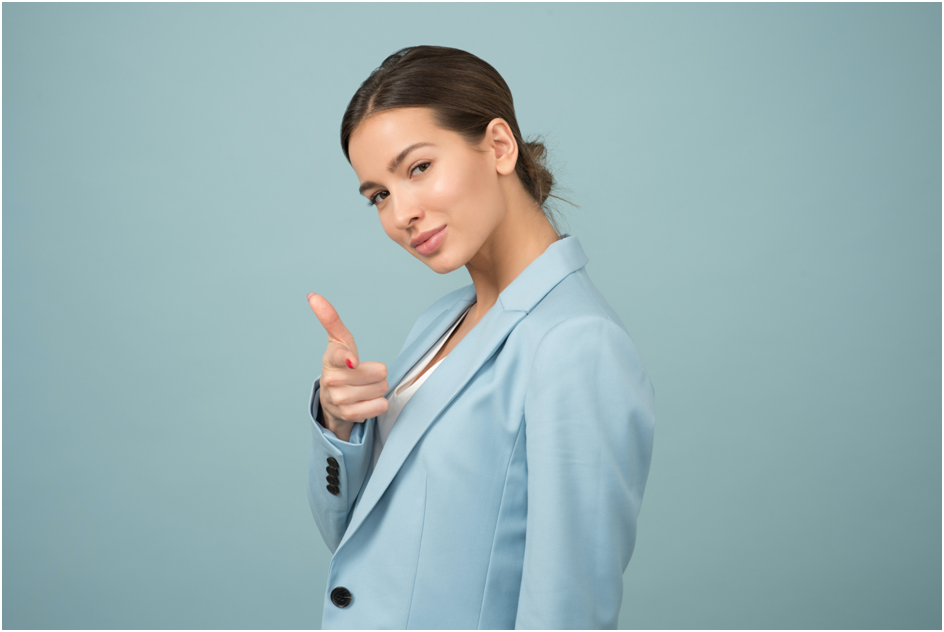 Confident looking young woman pointing her finger - wearing a pale blue blazer. dark hair tied back in a short ponytail.