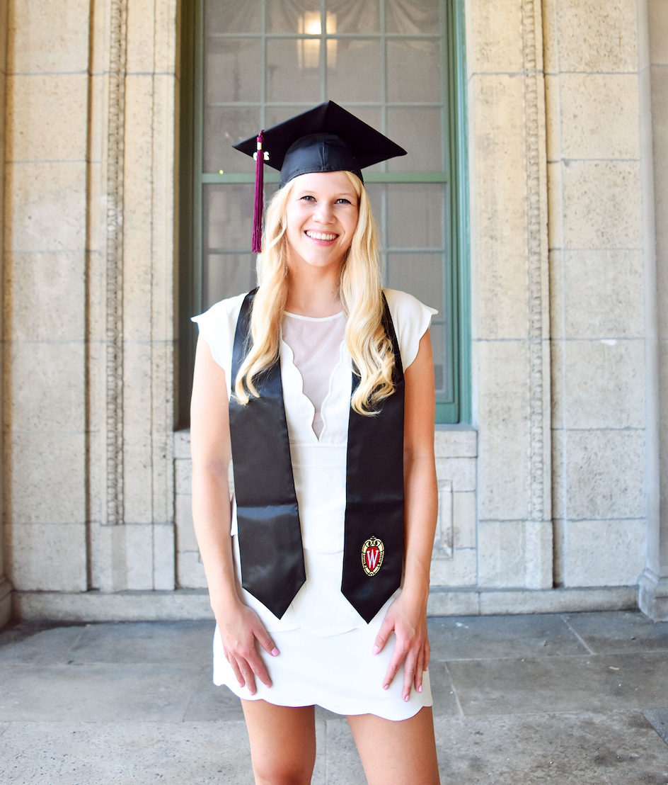 Jennifer Grissim is standing and looking at the camera wearing a graduation cap and stole over a white dress.