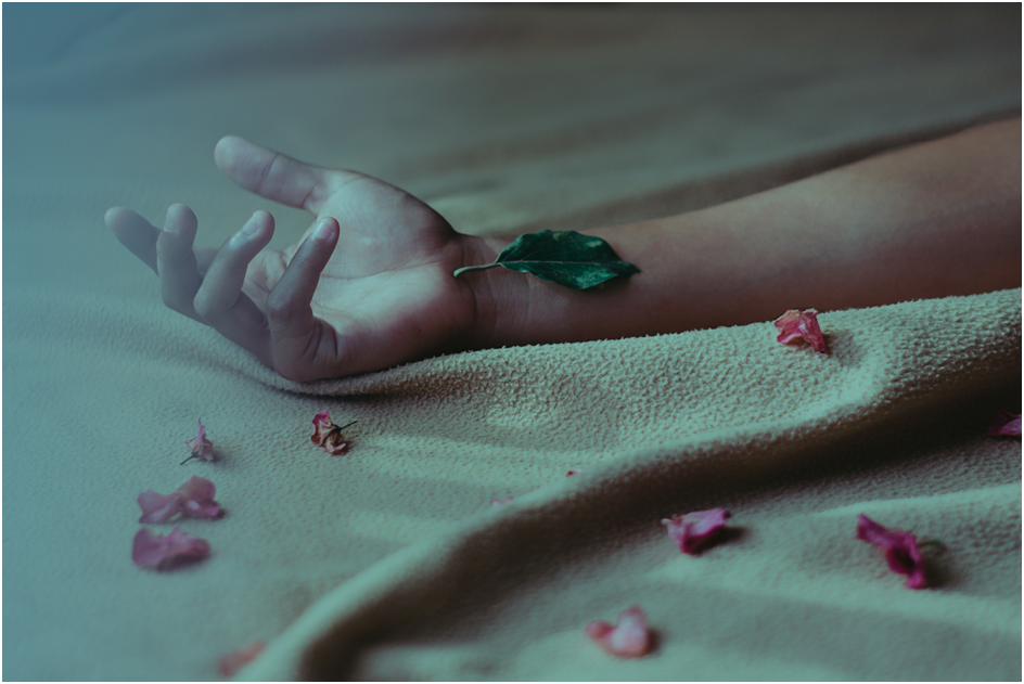 Extended arm showing up-turned hand with bent fingers across a green blanket surrounded by pink petals.