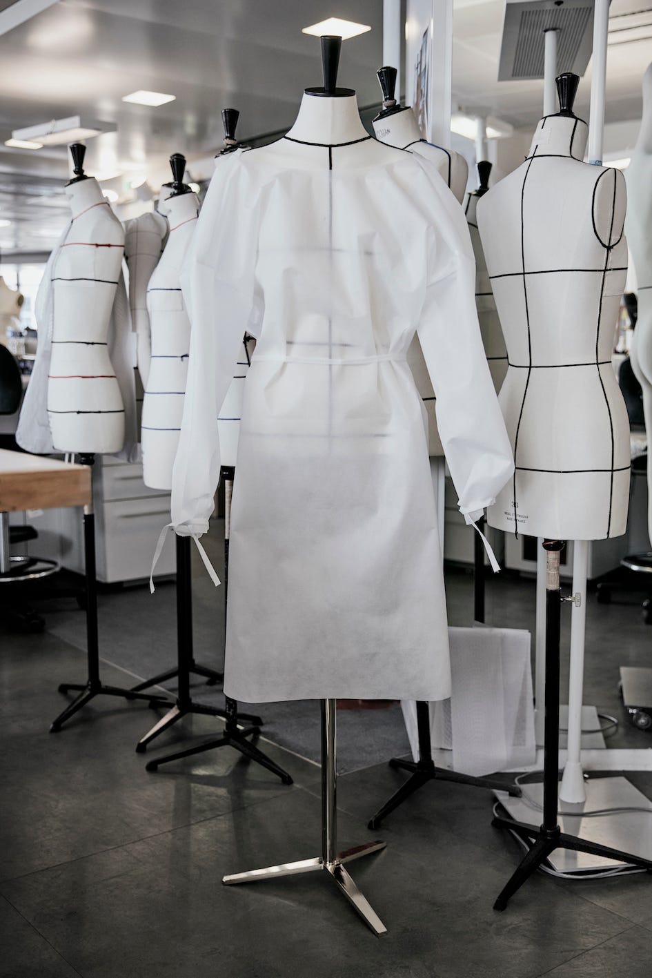 There are some fashion mannequins in a room. There is a white, rather transparent smock hanging on one of them.