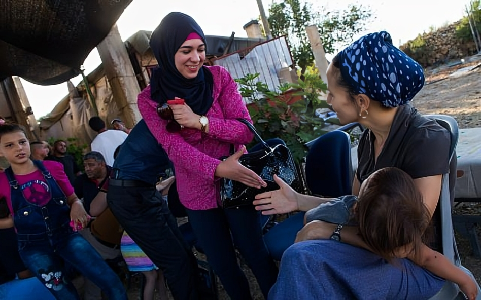 A picture of a Muslim and a Jewish Woman with a baby on her lap on the way to shake hands.