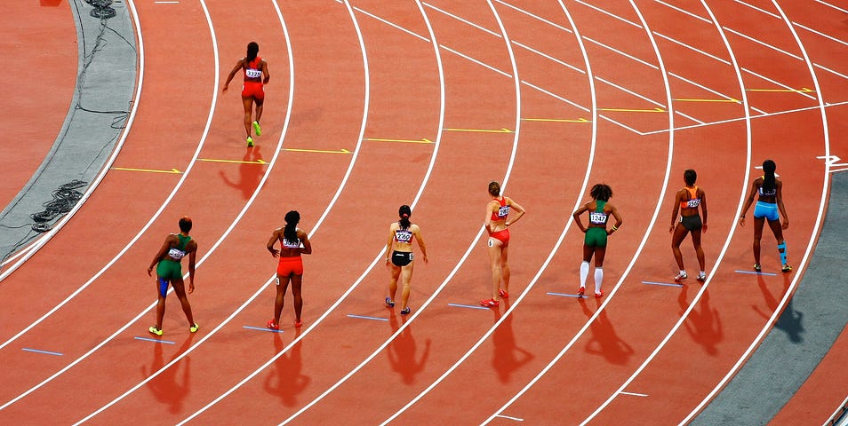 7 women line up to race on a formal athletics running track.