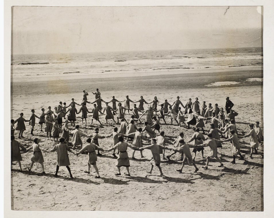 Large circles of children and adults in a formal game — on the beach