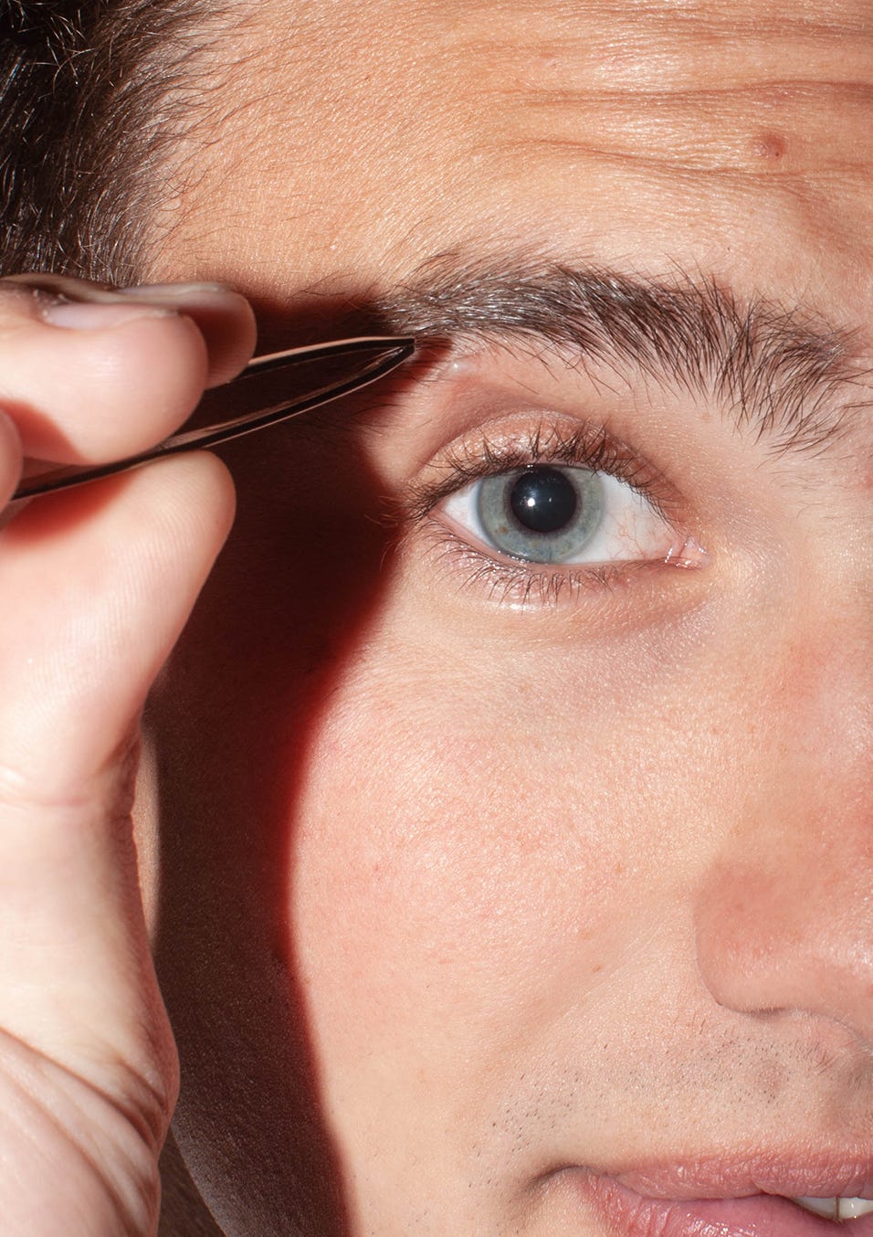 Man inspecting his skin and plucking his eyebrows. Skincare and self-care are for men, too!