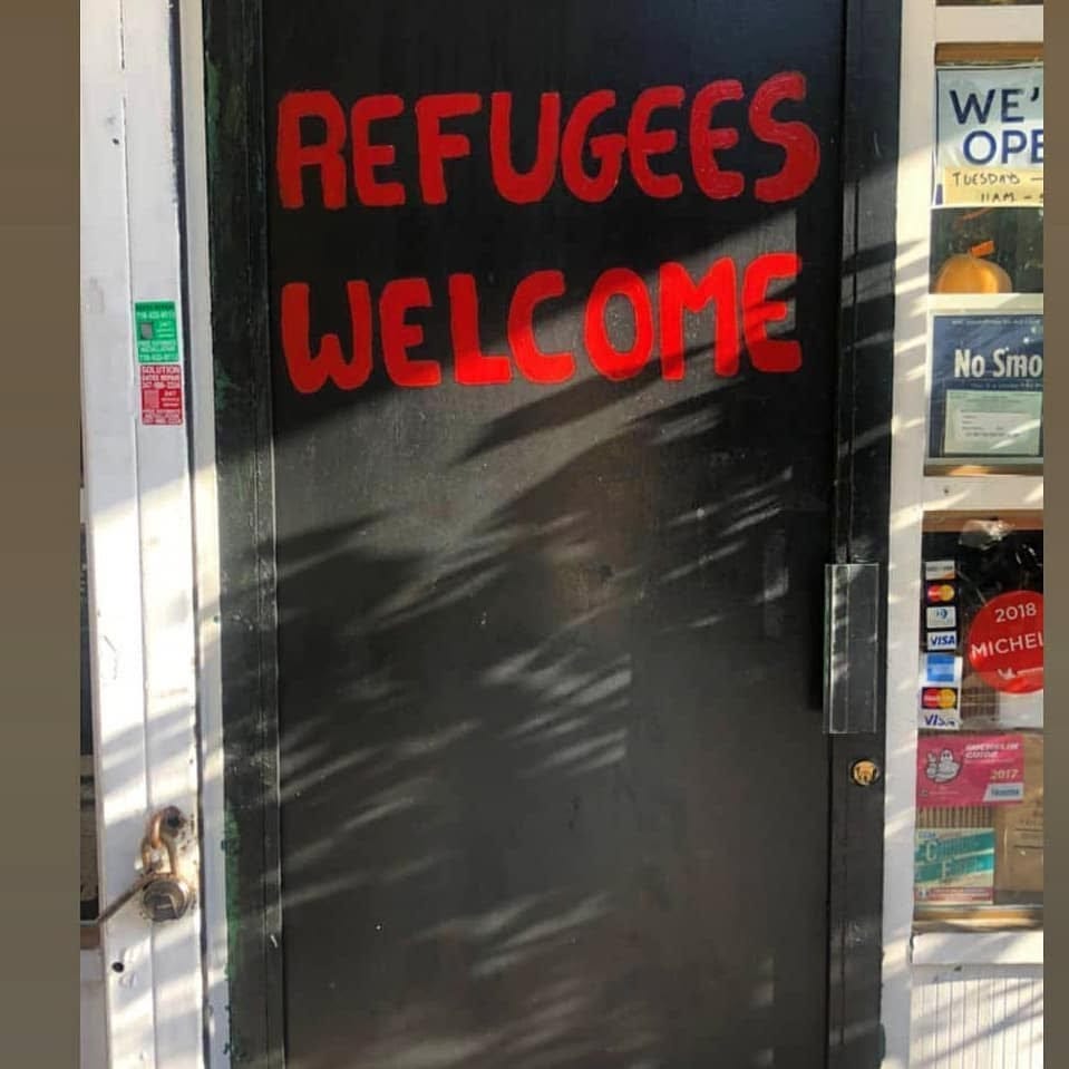 A door with the text “Refugees Welcomed” in red spray paint