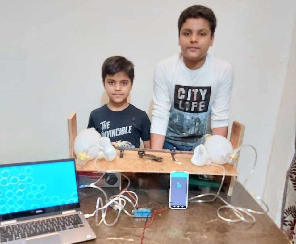 Two boys showing the wooden portable ventilator they developed, which is also connected to mobile app and a laptop.
