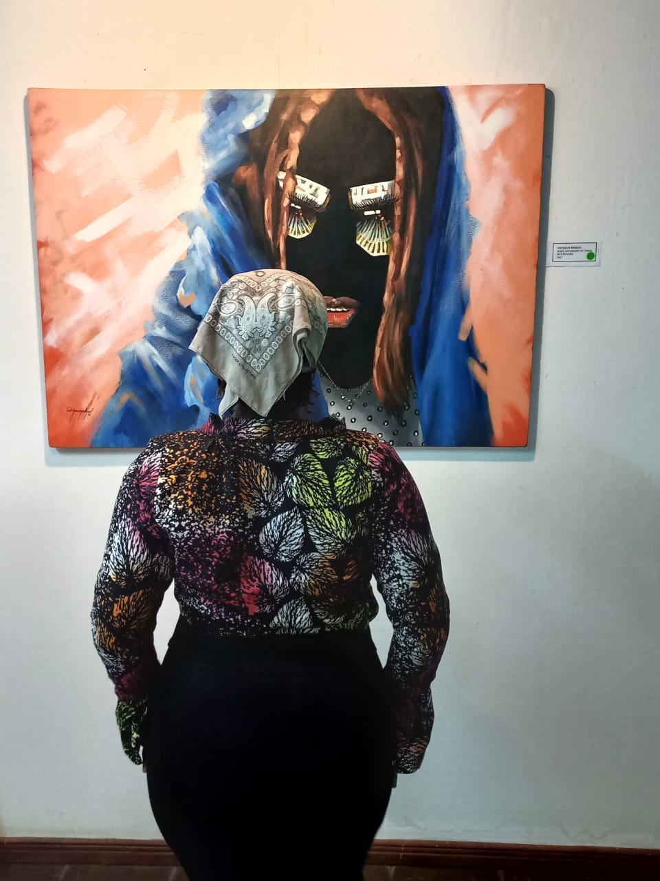 a lady in a leaf-patterned, long-sleeved blouse and bandana looking at a painting of a black lady Quazeem Animashaun