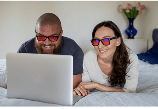 Couple with a laptop wearing pajama and blue light glasses having a movie marathon in bed
