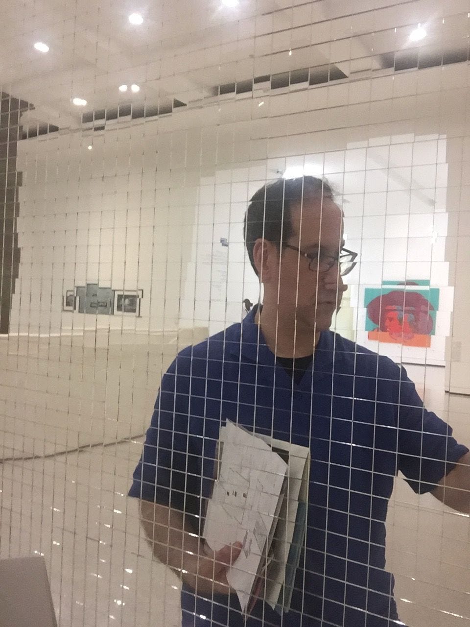 A man, holding papers, in front of a mirror made up of tiny squares