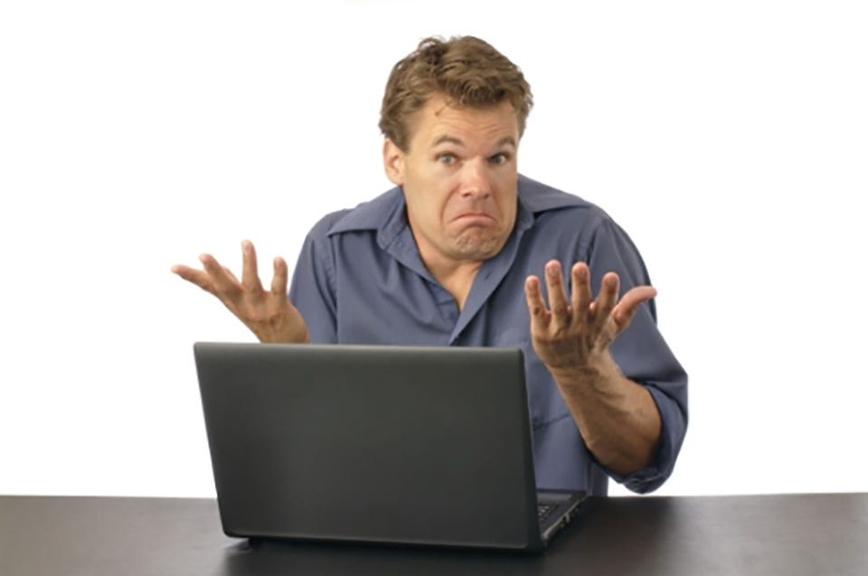 A generic stock image of an ordinary looking man in an ill-fitting shirt sitting at a computer screen, shrugging and making an exaggerated “I don’t know?” face.