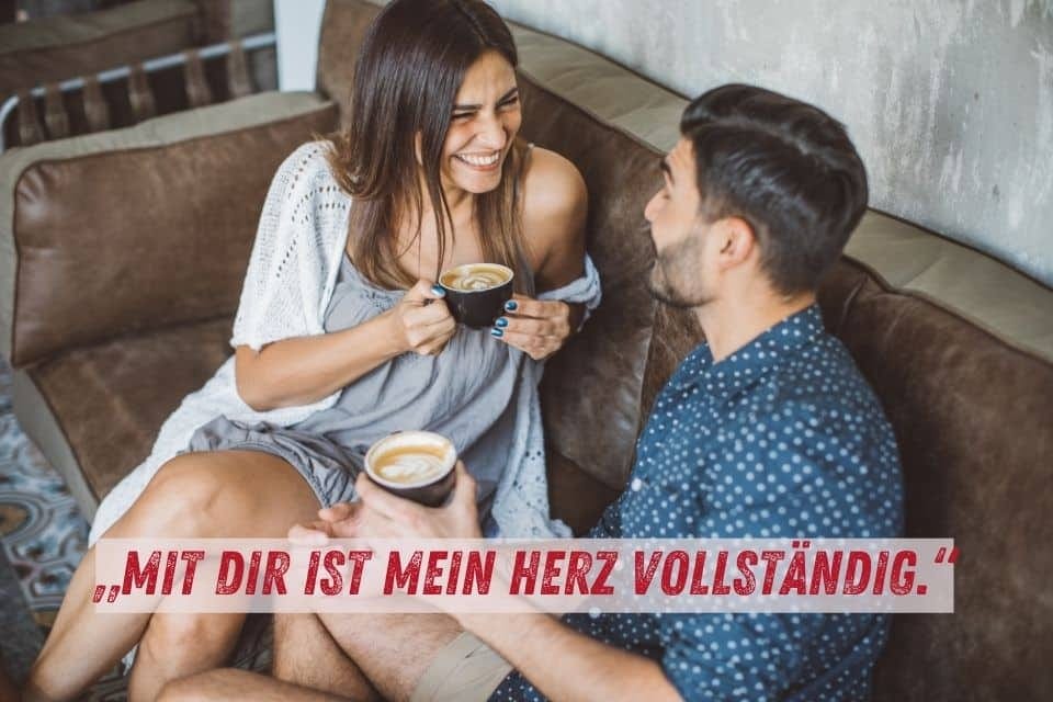 Auf dem Bild sitzt ein lachendes Paar auf einem braunen Sofa und genießt gemeinsam Kaffee. Die Frau trägt ein graues Kleid mit einem weißen Überwurf, der Mann ein blaues Hemd. Unten im Bild steht der Text: