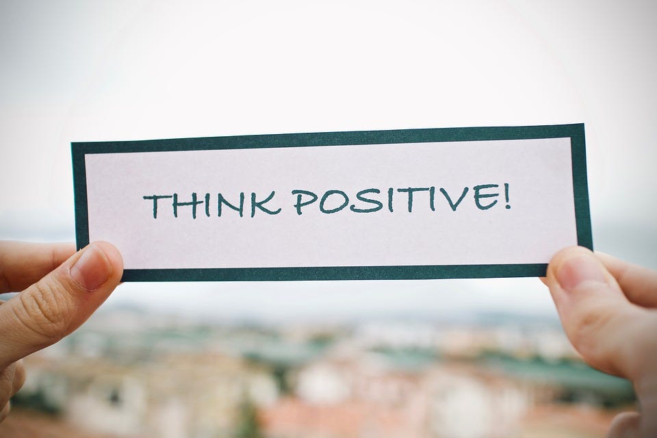 There is a piece of paper in someone’s hands which has text saying: “Think positive!”